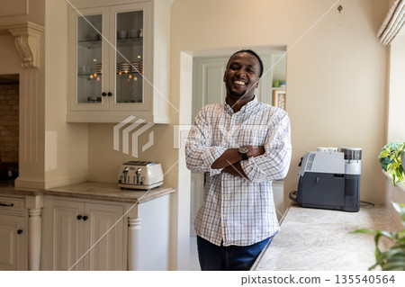 Smiling man standing in kitchen with arms crossed, enjoying relaxed morning 135540564