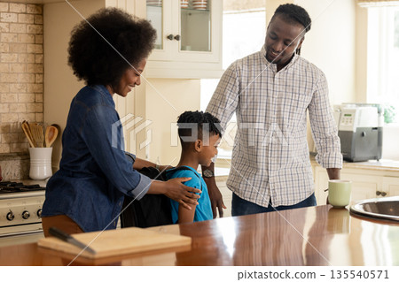 In kitchen, parents supporting child preparing for school with smiles and encouragement In kitchen, parents supporting child preparing for school with smiles and encouragement 135540571