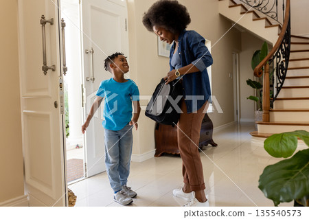 African American mother and son entering home, smiling and carrying backpack 135540573