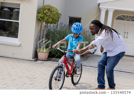 Father teaching son to ride bicycle on driveway, both enjoying moment Father teaching son to ride bicycle on driveway, both enjoying moment 135540574