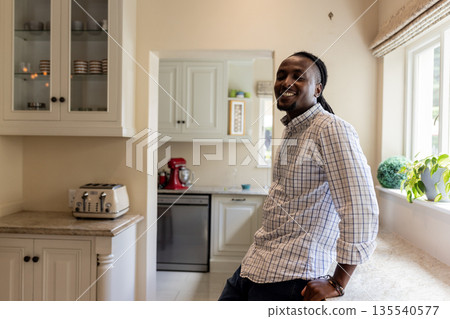 African American man smiling while leaning against kitchen counter at home African American man smiling while leaning against kitchen counter at home 135540577