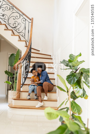 African American mother and child sitting on stairs, smiling and hugging at home African American mother and child sitting on stairs, smiling and hugging at home 135540585