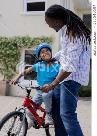 African American father teaching son to ride bicycle outdoors, both smiling happily African American father teaching son to ride bicycle outdoors, both smiling happily 135540594