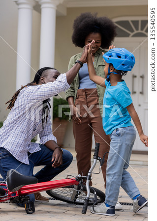 Family celebrating child's biking success with high five in front of house Family celebrating child's biking success with high five in front of house 135540595