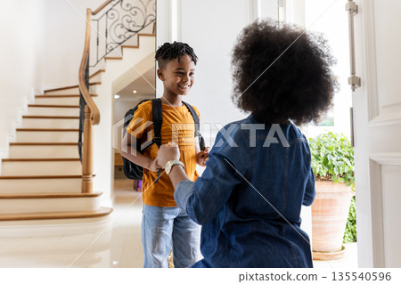 African American mother welcoming son home from school with warm embrace 135540596