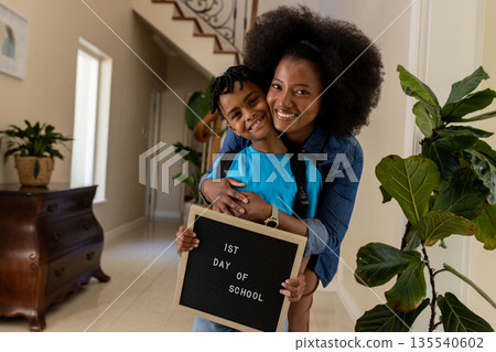 Mother and son smiling, holding sign for first day of school at home Mother and son smiling, holding sign for first day of school at home 135540602