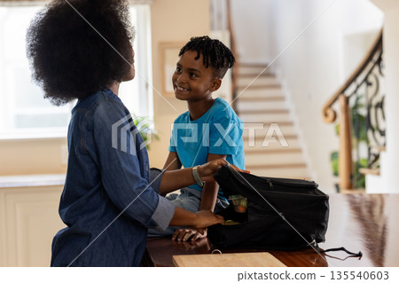 Mother and child packing backpack at home, sharing joyful moment together Mother and child packing backpack at home, sharing joyful moment together 135540603