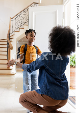 African American mother welcoming son with backpack at home, both smiling warmly 135540611