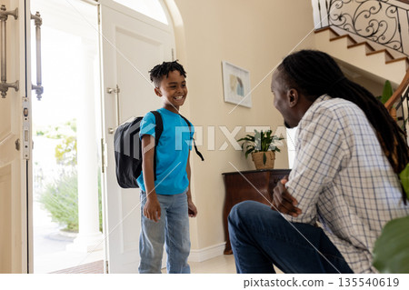 Father greeting son with backpack at home, sharing joyful moment by doorway Father greeting son with backpack at home, sharing joyful moment by doorway 135540619