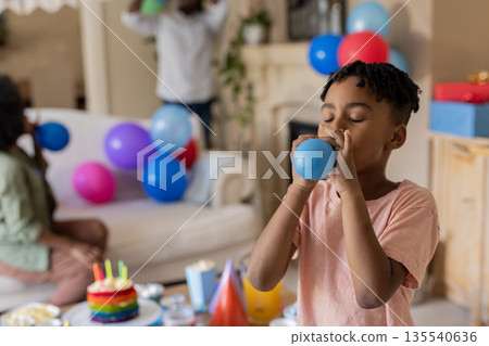 African American boy blowing up balloon at birthday party with family at home African American boy blowing up balloon at birthday party with family at home 135540636