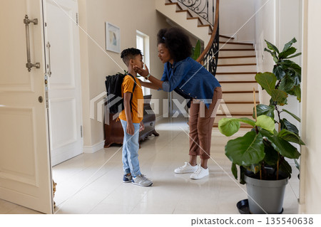 Mother gently adjusting son's backpack at home before school, sharing tender moment 135540638