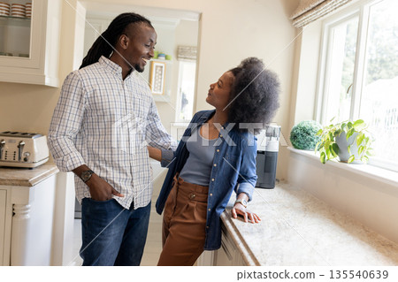 African American couple smiling and talking in kitchen near sunny window African American couple smiling and talking in kitchen near sunny window 135540639
