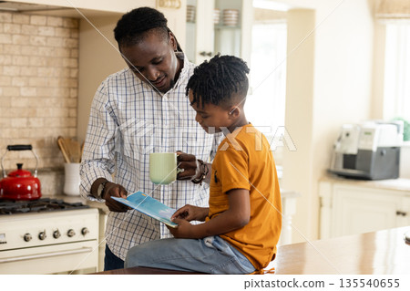 Reading book together in kitchen, African American father and son bonding Reading book together in kitchen, African American father and son bonding 135540655