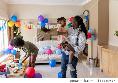 Father holding son while mother prepares birthday cake at home celebration 135540657