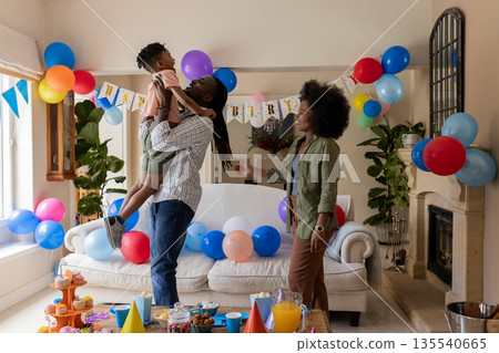 Father lifting son in air at birthday party, mother smiling in living room Father lifting son in air at birthday party, mother smiling in living room 135540665
