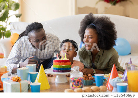 Family celebrating birthday at home, blowing out candles on colorful cake together 135540669