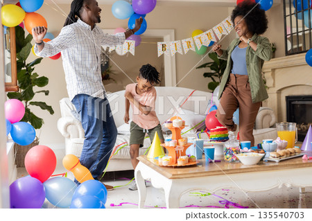 Celebrating birthday, family dancing joyfully among colorful balloons and home decorations 135540703