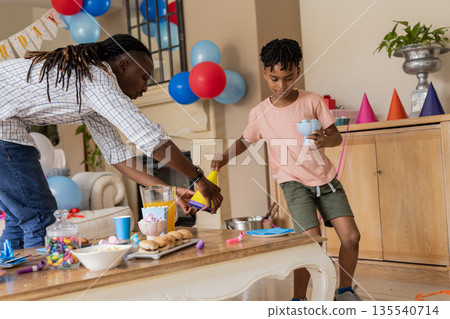Father and son preparing party table with snacks and colorful decorations at home 135540714
