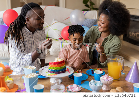 Celebrating birthday, parents and son enjoying rainbow cake and snacks at home Celebrating birthday, parents and son enjoying rainbow cake and snacks at home 135540721