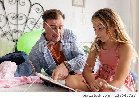 Father helping daughter with homework at home, both focused on learning Father helping daughter with homework at home, both focused on learning 135540728