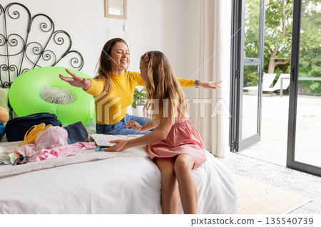 Mother and daughter joyfully packing clothes for vacation by poolside 135540739