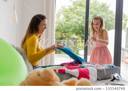 Mother and daughter joyfully packing suitcase together at home for vacation 135540748