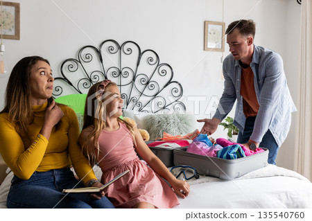 Family packing suitcase together on bed, preparing for vacation with excitement Family packing suitcase together on bed, preparing for vacation with excitement 135540760