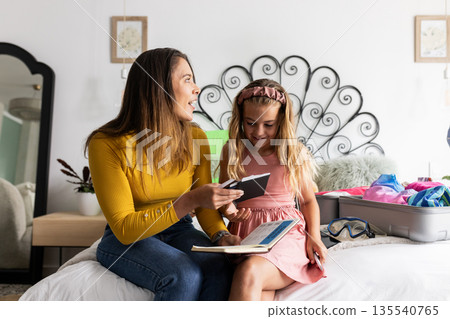 Mother and daughter packing suitcase together, smiling and sharing joyful moment 135540765