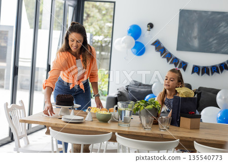 Celebrating birthday, woman placing cake on table while girl eagerly watching 135540773