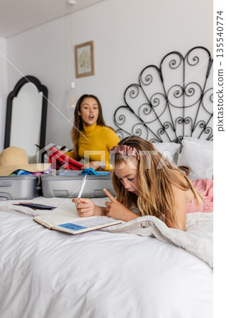 Packing suitcase on bed, mother and daughter writing in notebook for trip Packing suitcase on bed, mother and daughter writing in notebook for trip 135540774