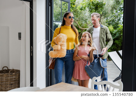 Family arriving home with bags and teddy bear, smiling and chatting together 135540780