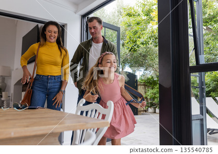 Happy family entering home, young girl joyfully leading parents through doorway 135540785