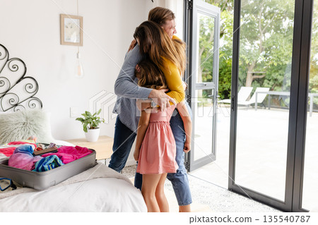 Family embracing warmly near open patio door, suitcase on bed, enjoying togetherness Family embracing warmly near open patio door, suitcase on bed, enjoying togetherness 135540787