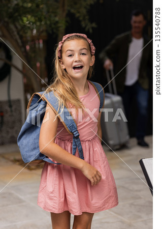 Excited girl with backpack smiling while father arrives with suitcase at home Excited girl with backpack smiling while father arrives with suitcase at home 135540788