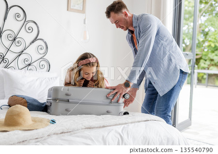 Father and daughter packing suitcase on bed, preparing for family vacation 135540790