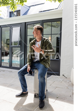 Man sitting outdoors on suitcase, holding smartphone, enjoying sunny day Man sitting outdoors on suitcase, holding smartphone, enjoying sunny day 135540801