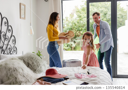 Family packing for vacation, smiling and organizing clothes on bed at home 135540814