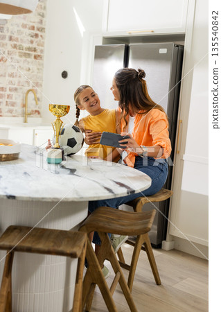 Celebrating soccer trophy, mother and child sharing joyful moment at kitchen counter Celebrating soccer trophy, mother and child sharing joyful moment at kitchen counter 135540842