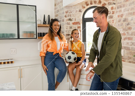 In kitchen, family sharing playful moment, daughter holding soccer ball, smiling 135540867