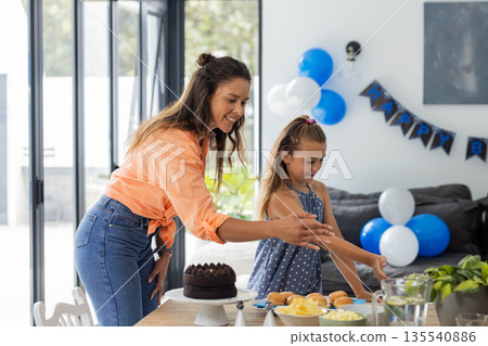 Mother and daughter preparing birthday table with cake and decorations at home Mother and daughter preparing birthday table with cake and decorations at home 135540886