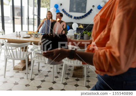 Celebrating birthday, person carrying cake with lit candles towards family at home 135540890