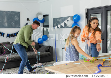 Family cleaning up after birthday party at home, surrounded by decorations 135540898