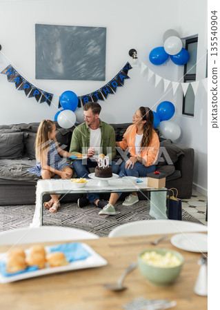 Celebrating birthday, family sitting on sofa with cake and decorations at home 135540904