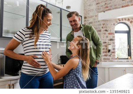 Happy family bonding in kitchen, young girl touching mother's pregnant belly 135540921