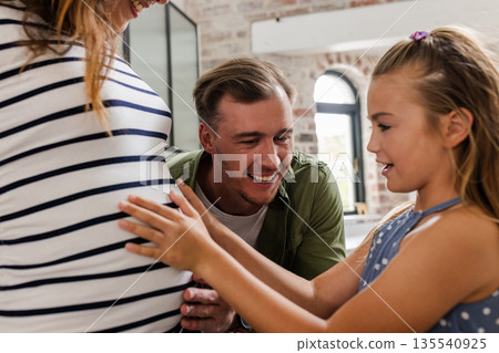 Smiling family bonding, young girl touching pregnant mother's belly at home 135540925