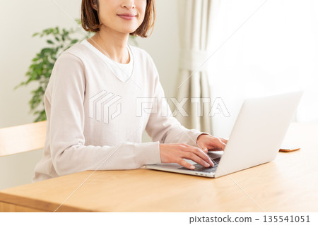 一位中年婦女在家裡的客廳看著電腦。 135541051