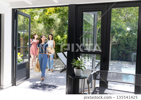 Walking through open doors, three young women enter sunlit patio area Walking through open doors, three young women enter sunlit patio area 135541425