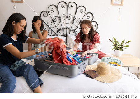 Packing clothes into suitcase, three women prepare for sunny vacation 135541479