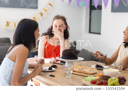 Laughing and enjoying cake, three young women gather at birthday celebration Laughing and enjoying cake, three young women gather at birthday celebration 135541504