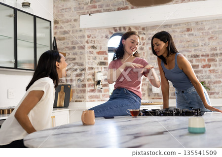 Laughing and chatting, three young women gather in cozy kitchen setting 135541509